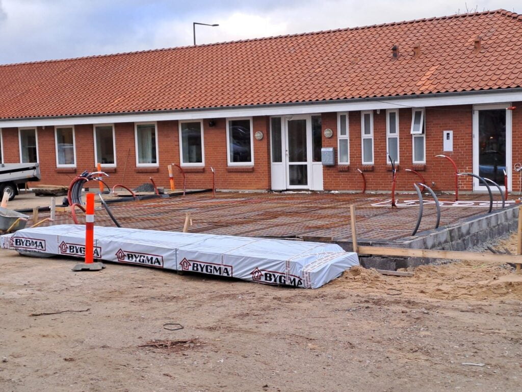 Husbyggeri med armering og rørinstallation foran bygning