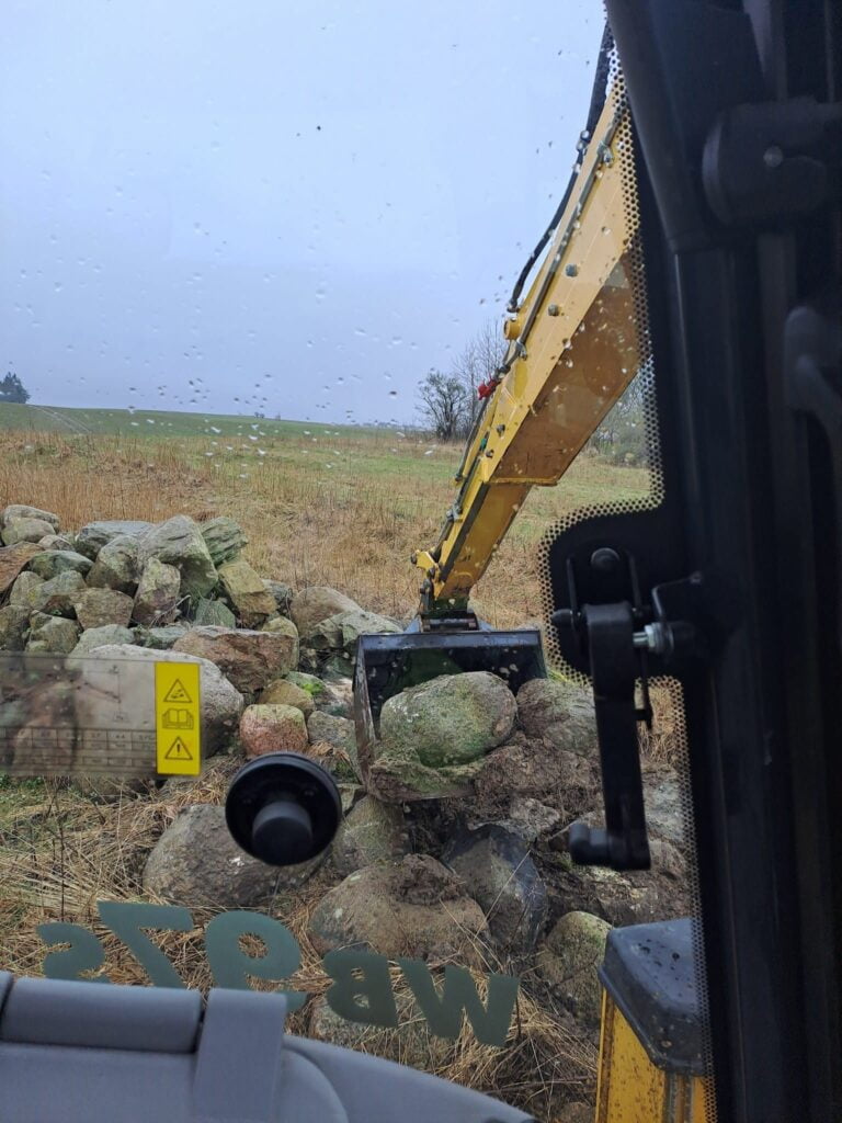 Gravemaskine flytter store sten på marken
