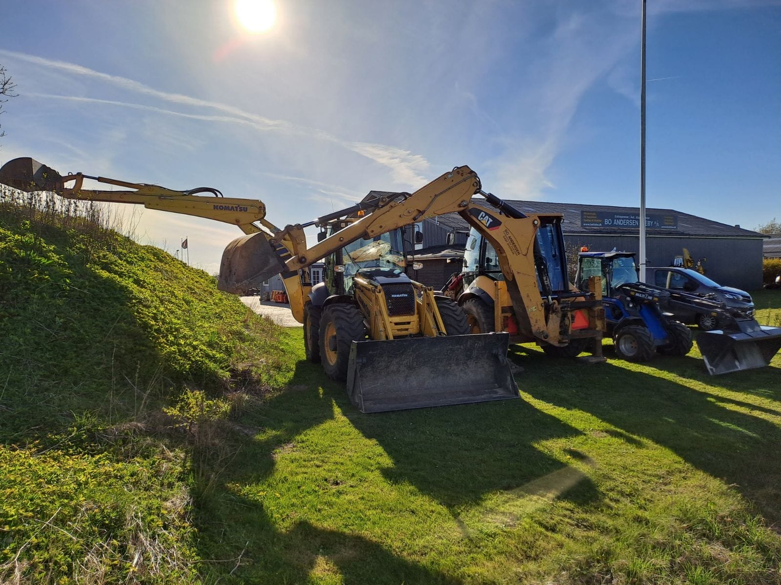Gravemaskiner og traktorer parkeret ved maskinværksted