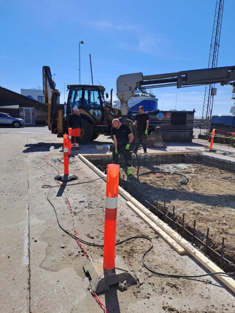 Arbejdere ved byggeplads med gravemaskine og betonpumpe