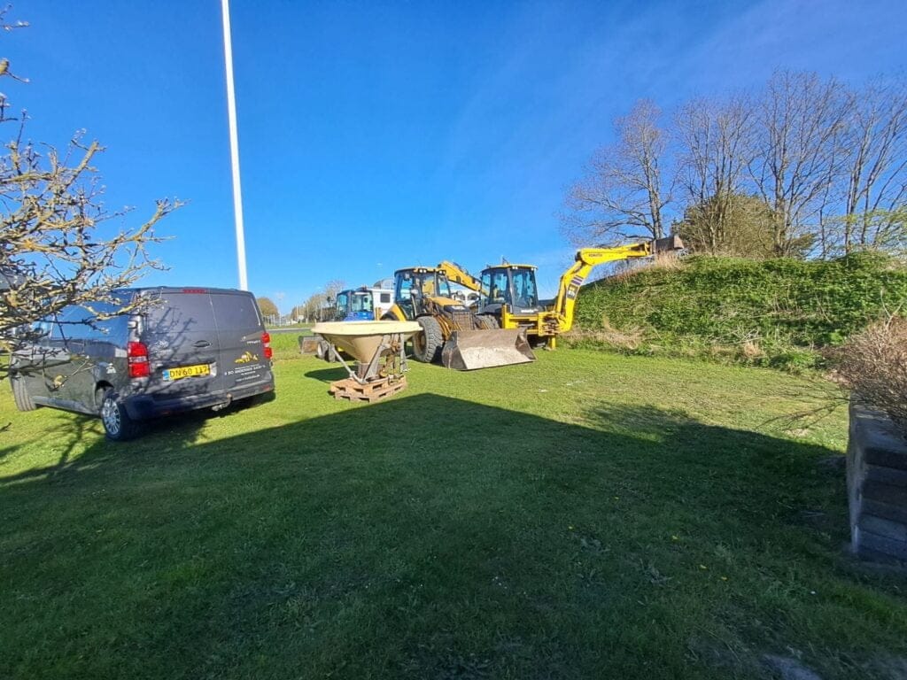 Gravemaskiner og varevogn på græsplæne under blå himmel