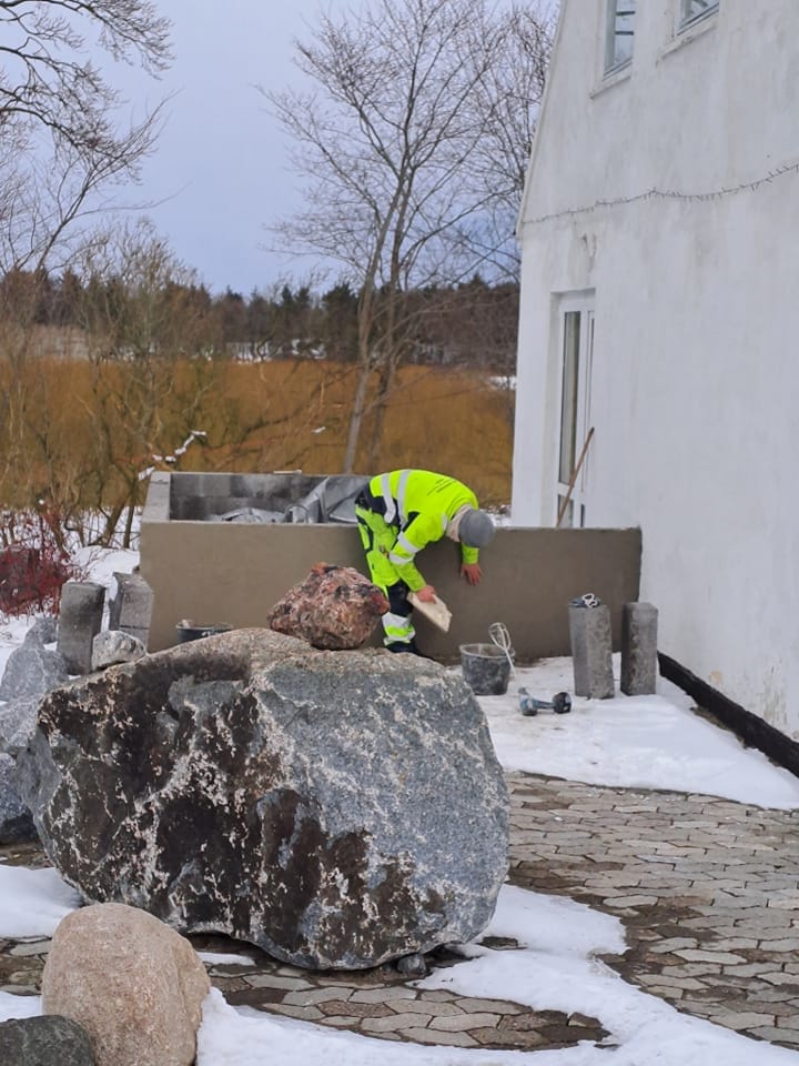 Arbejder pudser mur ved hus om vinteren